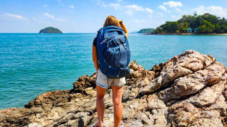 Beitragsbild von einem Mädchen, dass nur mit Handgepäck reist und mit einem blauen Rucksack am Meer steht